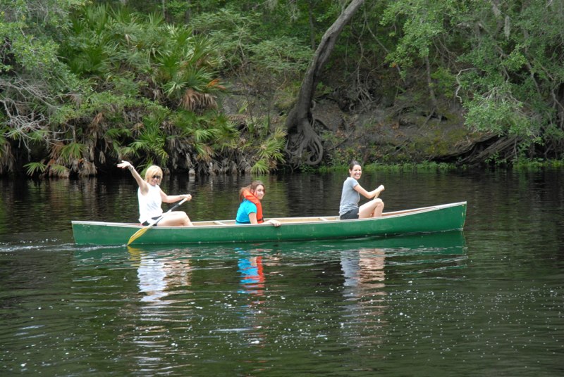 Campers canoeing along a lush riverbank